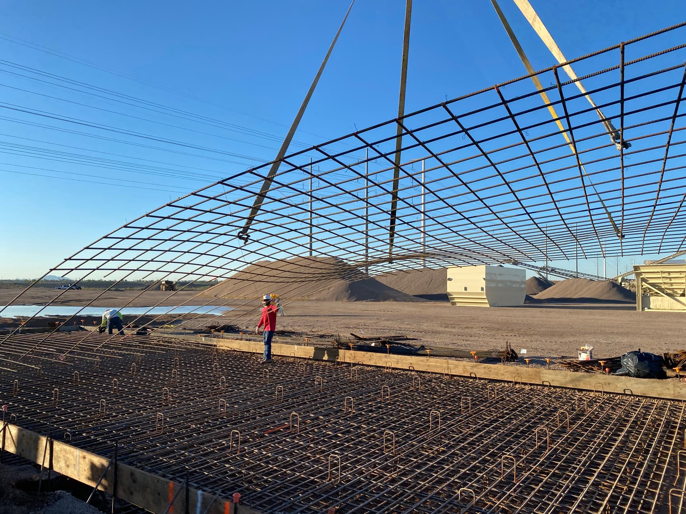 A large curved reinforcing cage standing against the sky before placement