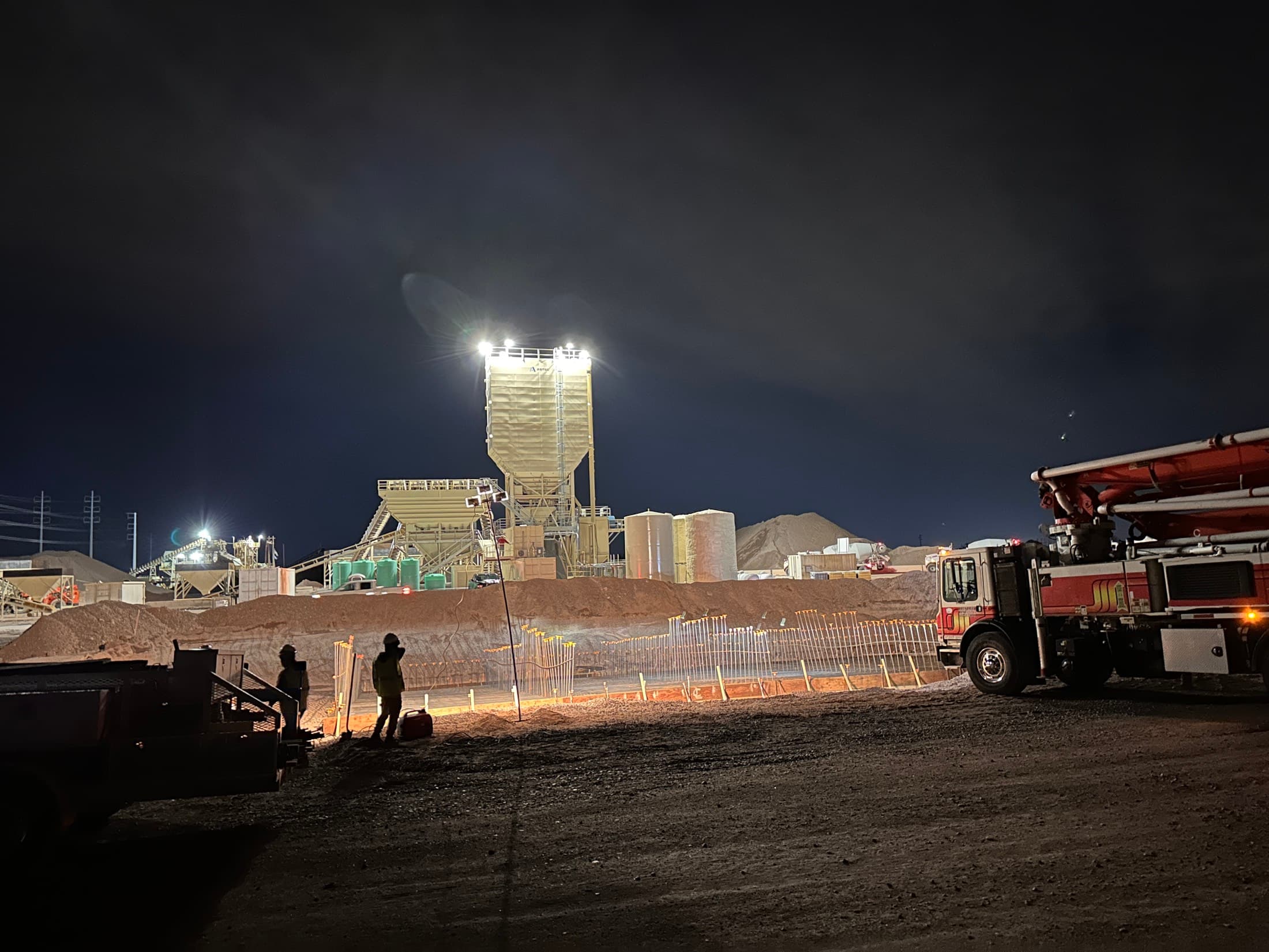 Concrete pump running at night alongside a lit plant during a scheduled shutdown