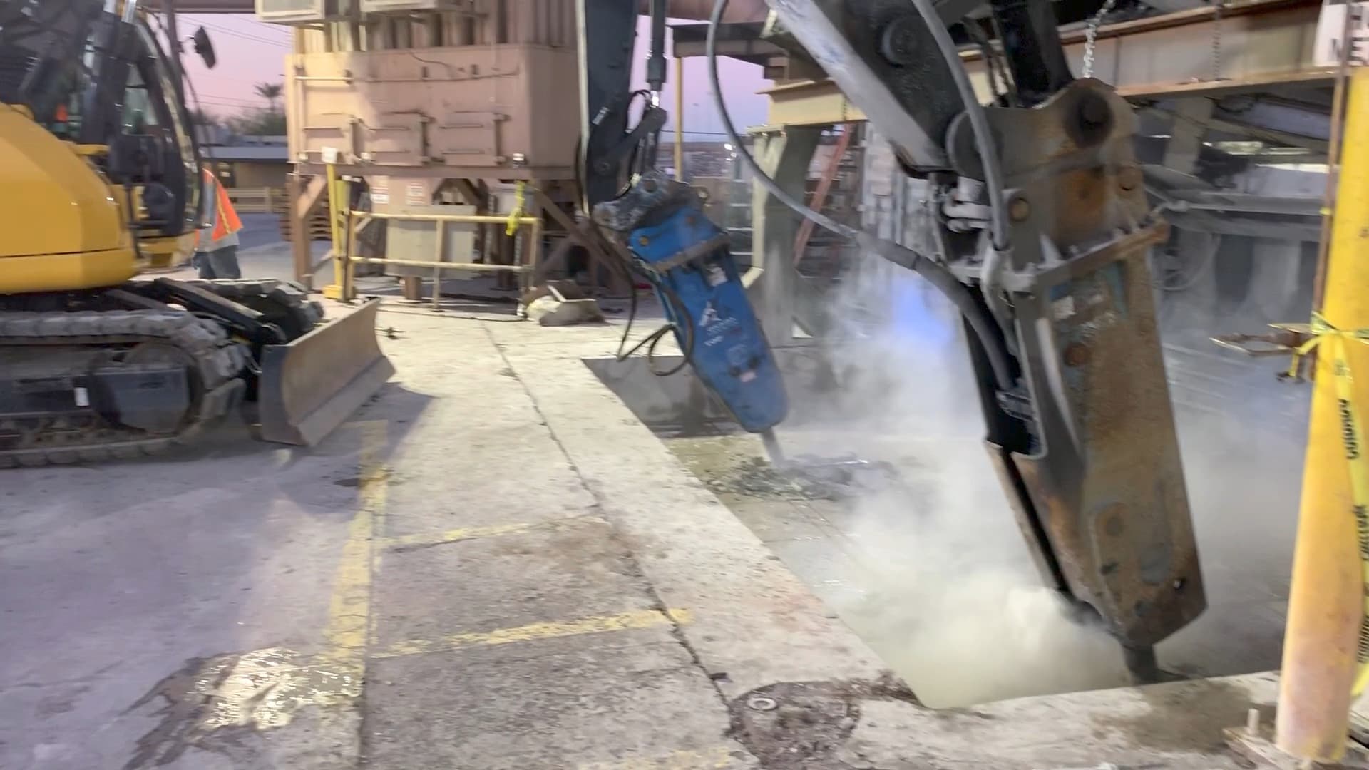 Two excavator-mounted hydraulic breakers working the same foundation at once, dust rising, at first light